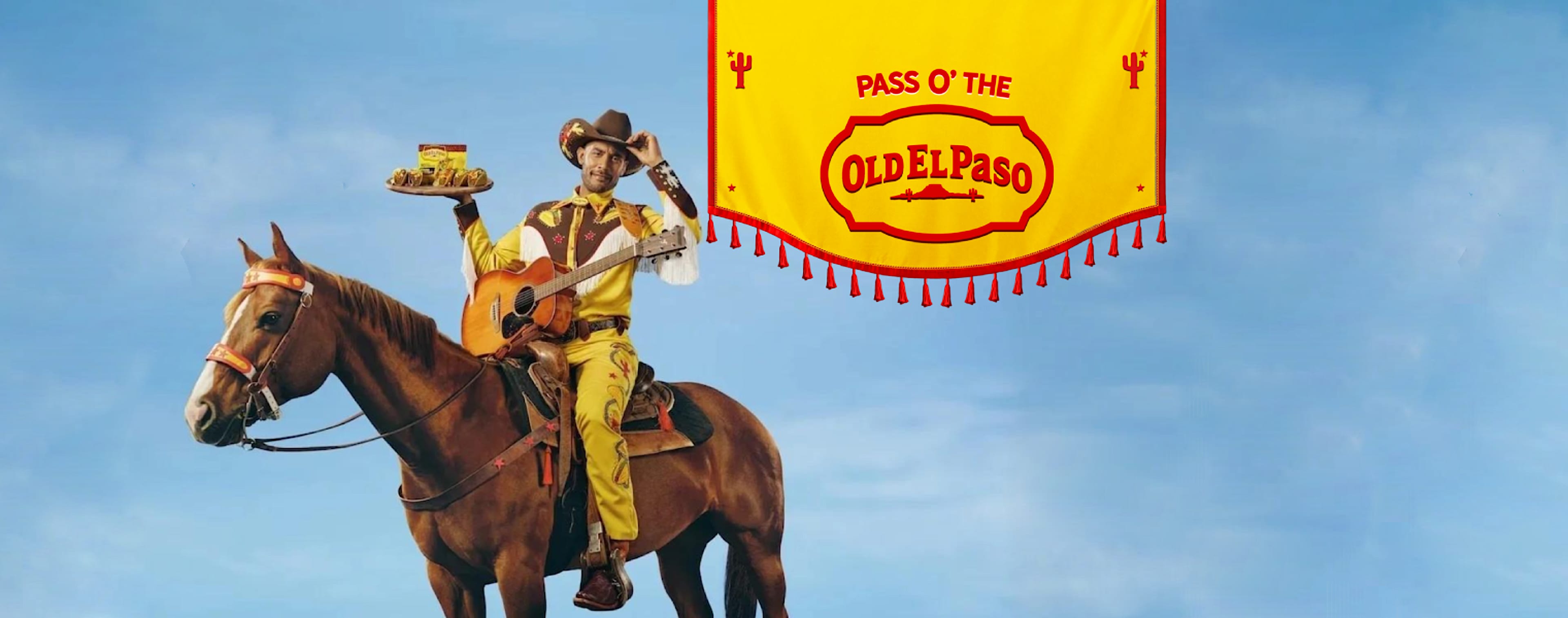 Cowboy sitting on a brown horse, holding a tray of tacos in one hand while his other hand is on his hat; a guitar is strapped to his front. A yellow banner in the background reads 'PASS O' THE OLDEL PASO' in red text.